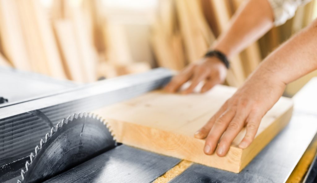 Worker hands details of wood cutter machine with a circular saw